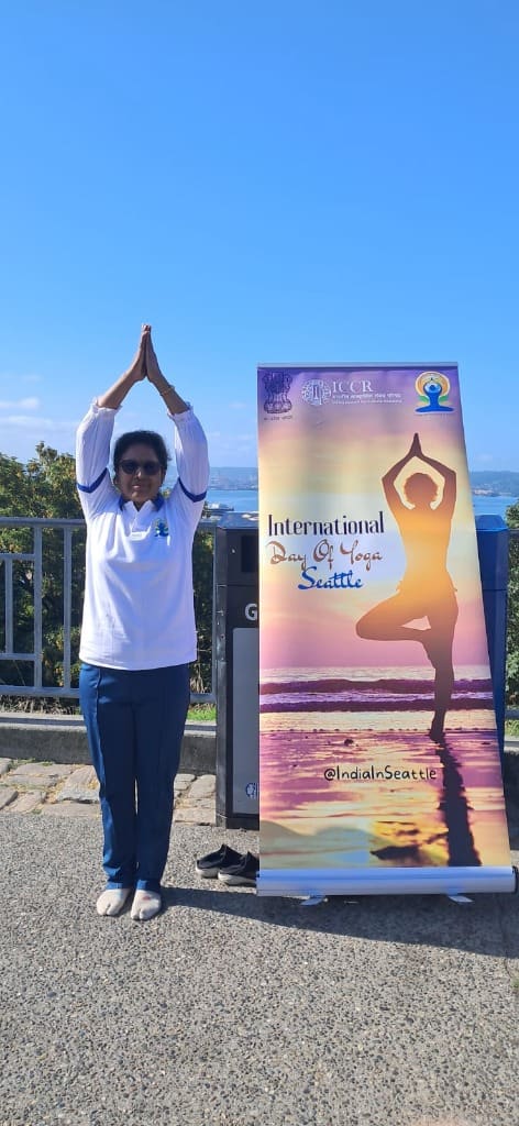 Dr. Seema Saxena in tree pose beside an International Day of Yoga banner in Seattle